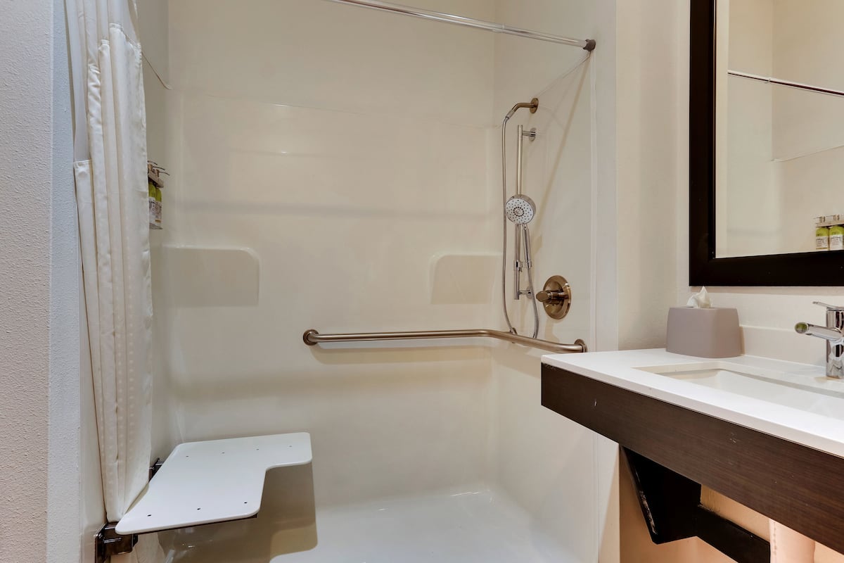 A bathroom with a white bathtub, a shower with a handheld showerhead, a grab bar, a towel rack, and a mirror above the sink.