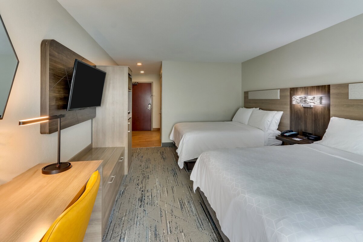 A hotel room with a bed, bedside table, TV, and a desk with a chair.