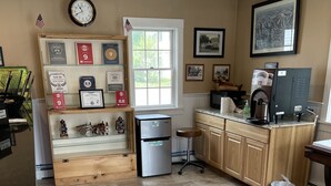 Una cocina con refrigerador, cafetera y ventana. Hay premios enmarcados en la pared y un reloj sobre la ventana.