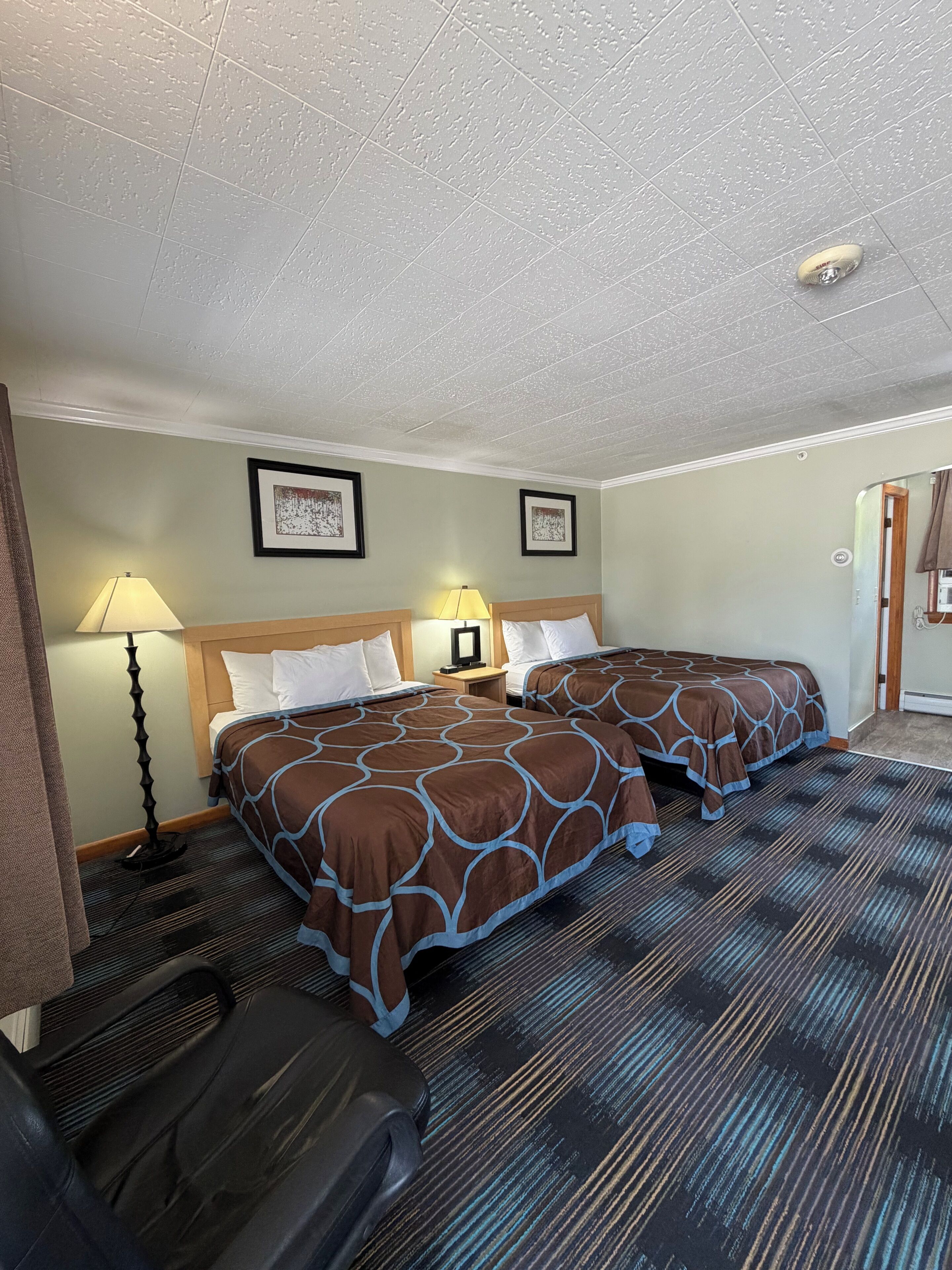 A hotel room with two beds, a desk, a lamp, and a suitcase.