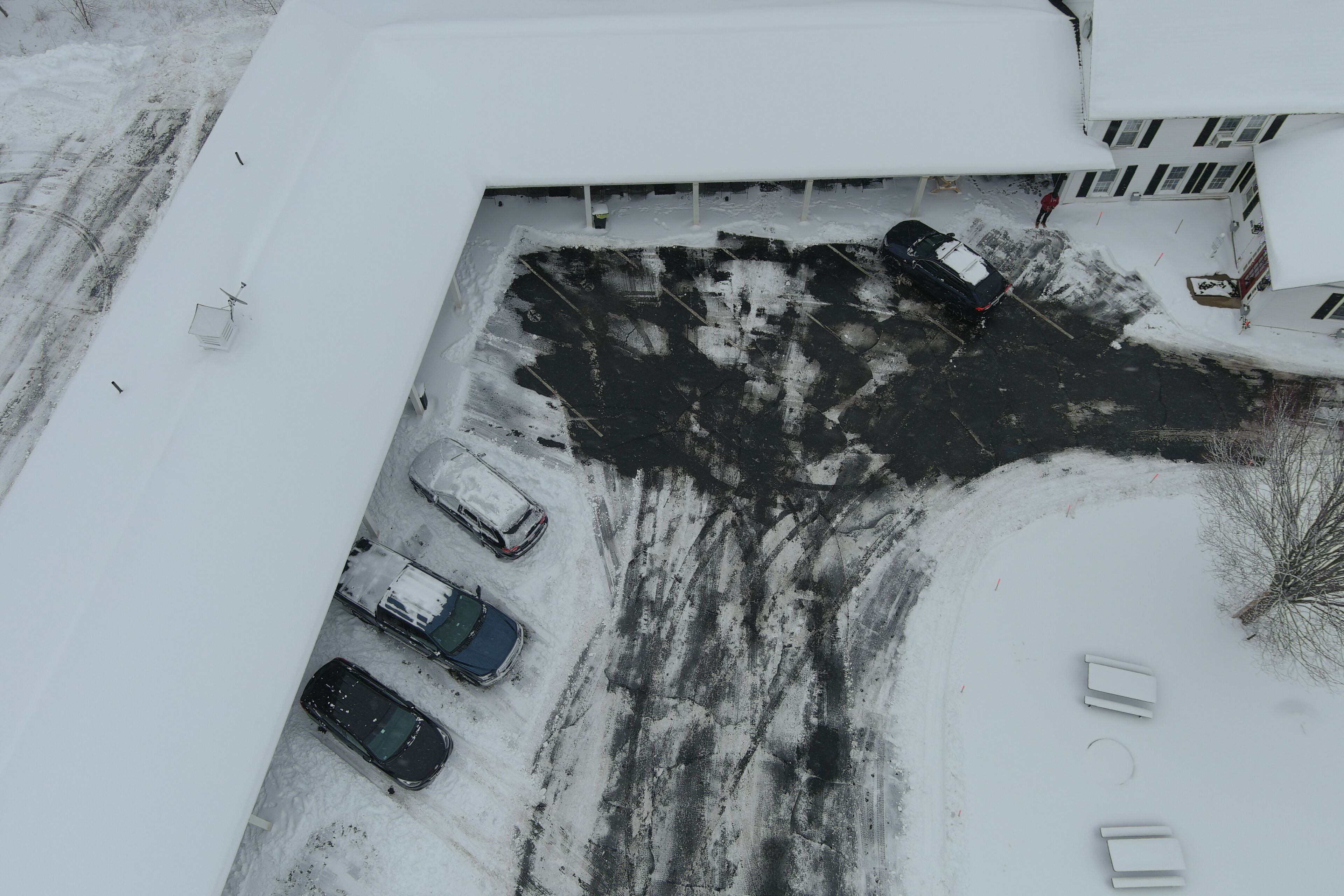An aerial view of a parking lot with several cars parked, surrounded by snow-covered ground and buildings.