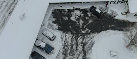 Vista aérea de un estacionamiento con varios autos estacionados, rodeado de terreno cubierto de nieve y edificios.