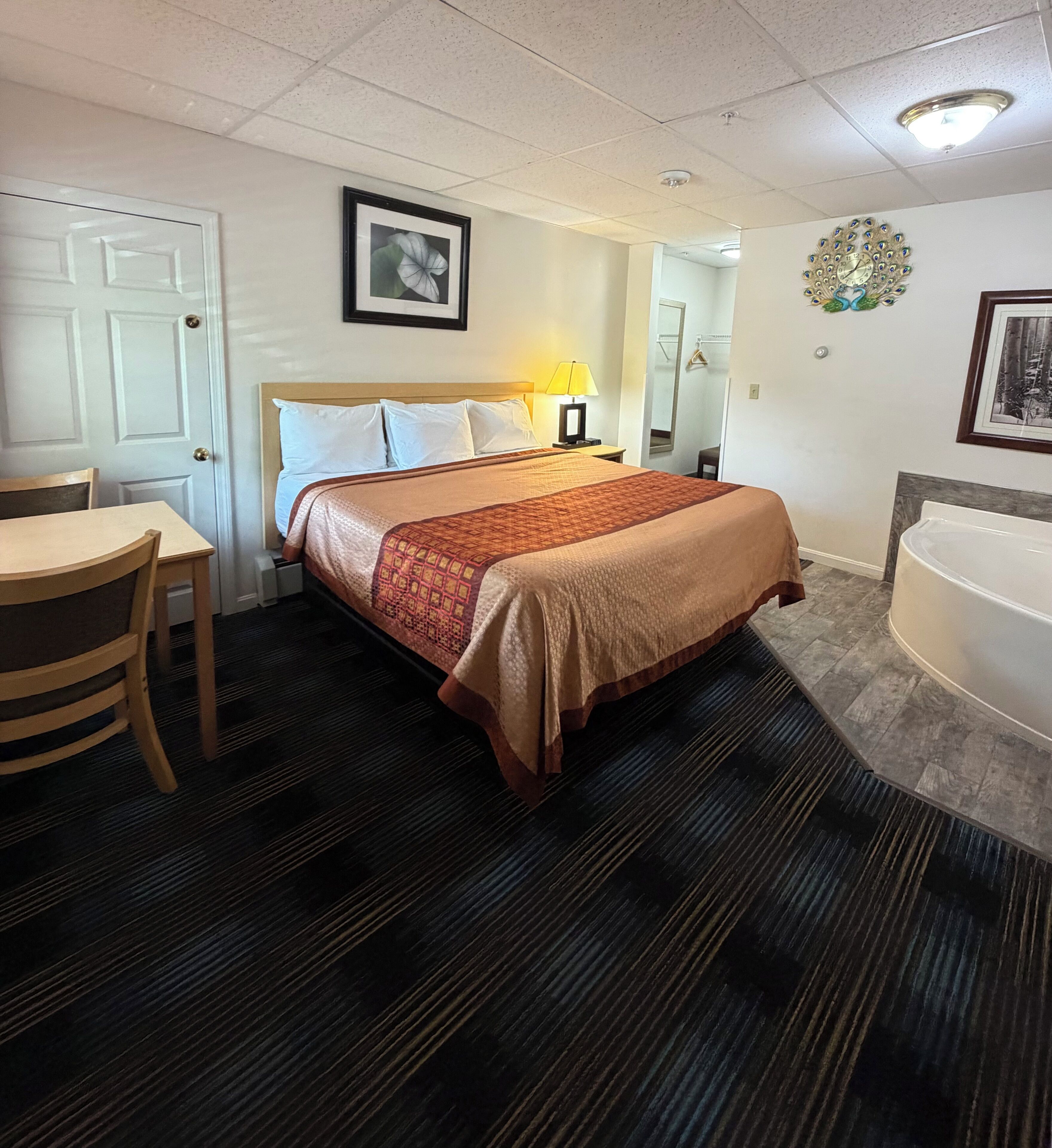 A hotel room with a bed, a desk, a chair, a bathroom with a bathtub, and a clock on the wall.