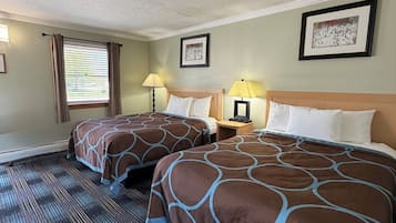 Ett hotellrum med två sängar, ett fönster med gardiner, en sänggavel, ett nattduksbord med en lampa och en inramad tavla på väggen.