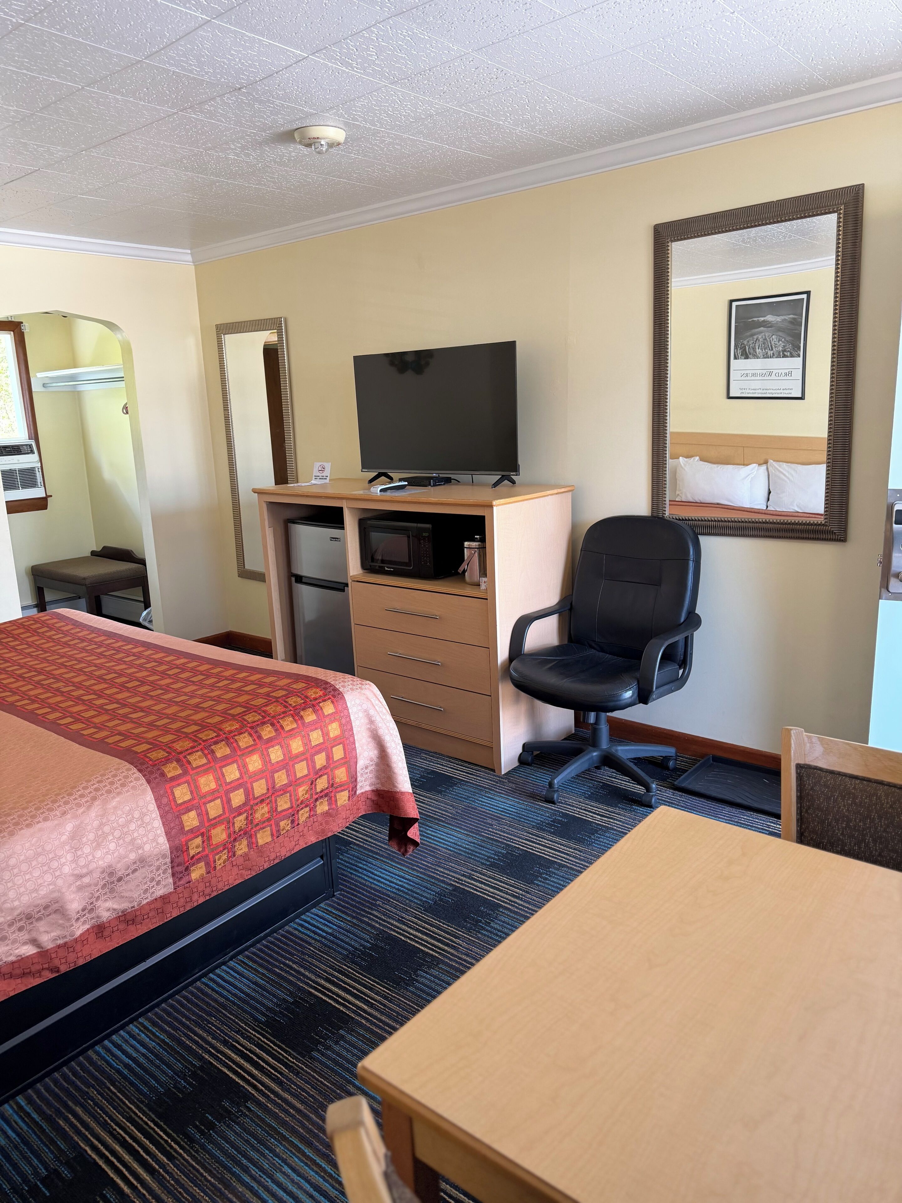 A hotel room with a bed, desk, chair, television, and a microwave.