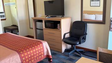 A hotel room with a bed, desk, chair, television, and a microwave.