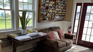 Una sala de estar con un sofá de cuero marrón, una mesa de centro con libros, una planta en maceta y una estantería llena de revistas.
