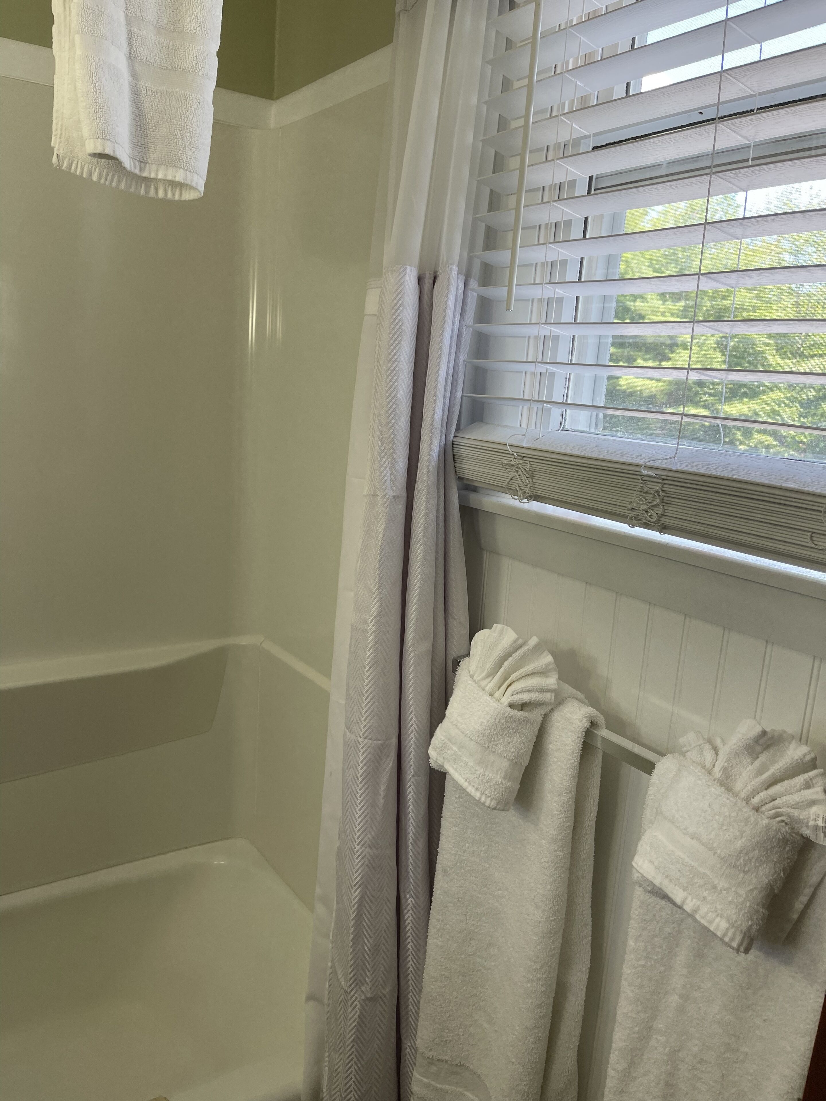 Une salle de bain avec une douche, une fenêtre avec des stores et des serviettes suspendues sur un porte-serviettes.
