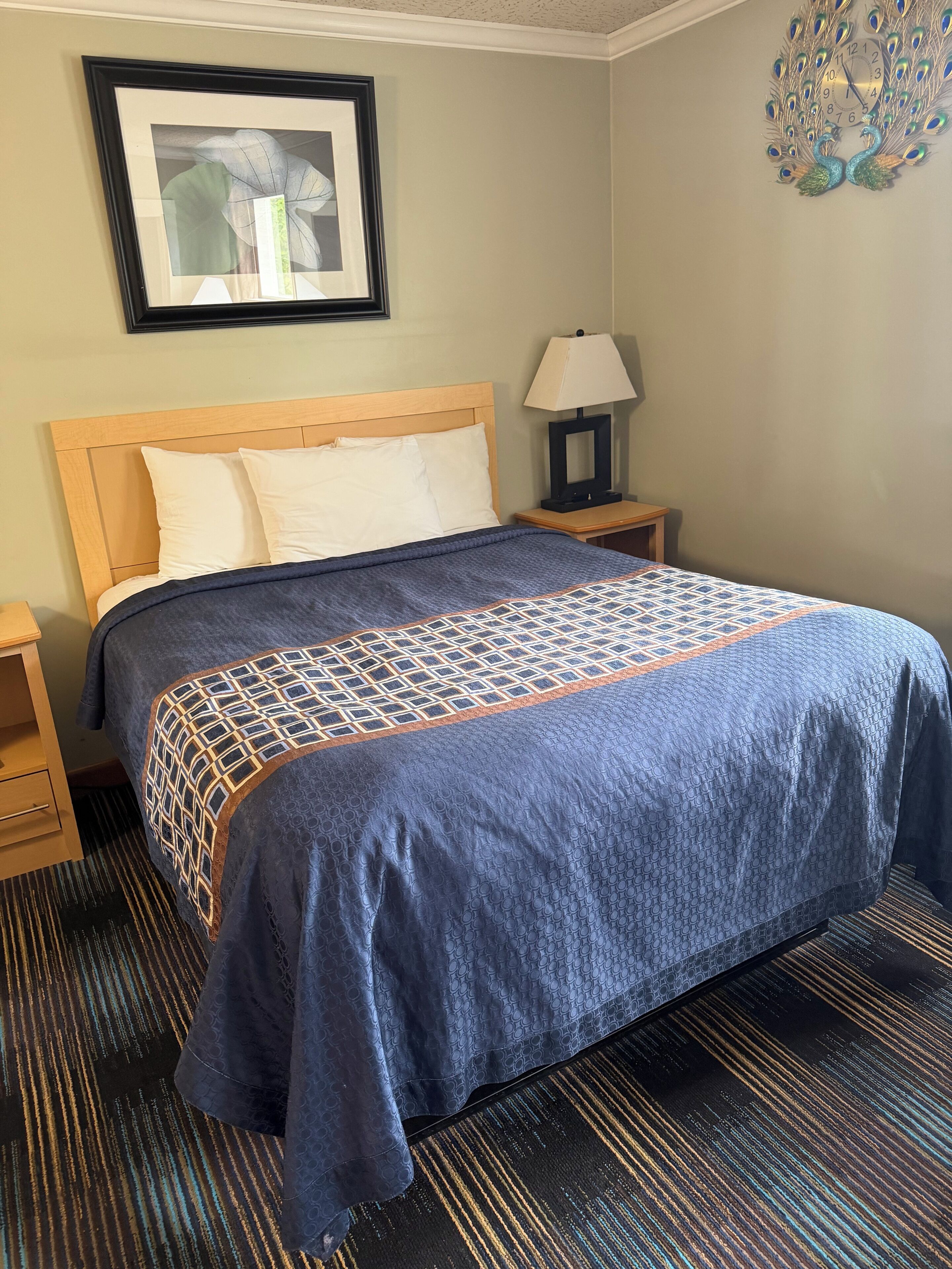 Una habitación de hotel con una cama, una mesita de noche, una lámpara, un cuadro enmarcado en la pared y un adorno mural.
