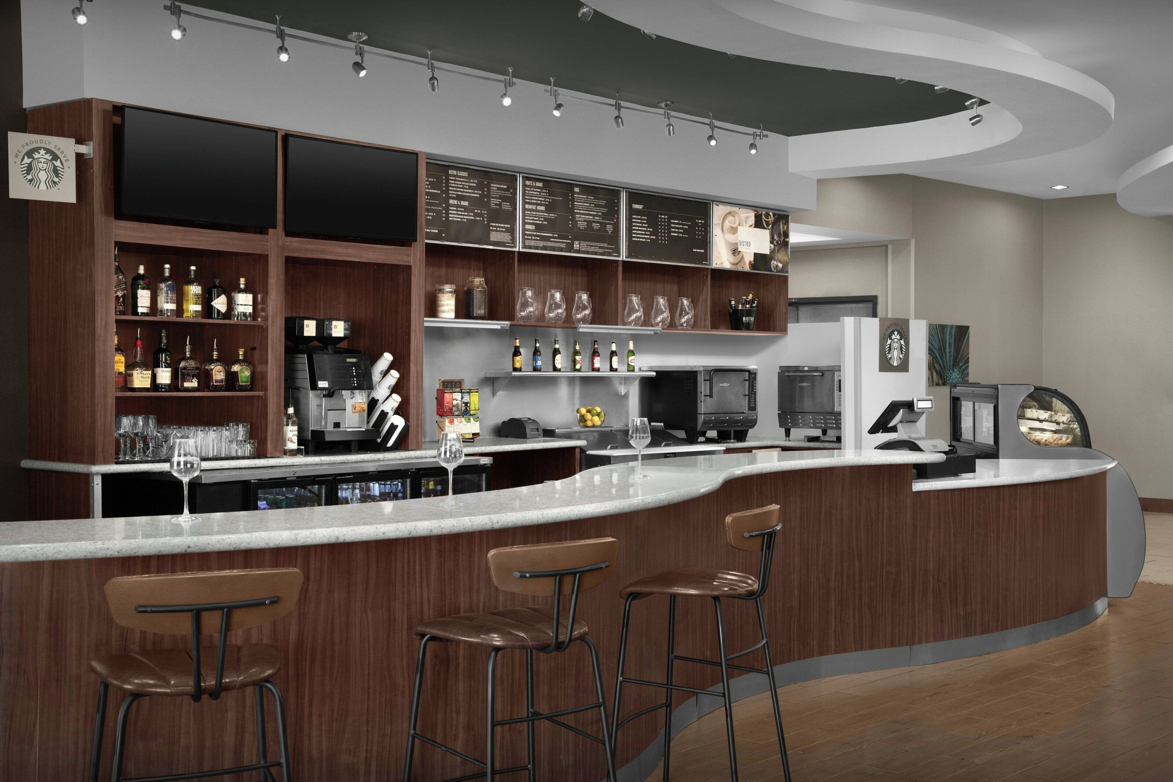 Zona de bar moderna con una barra curva, taburetes y una variedad de bebidas y cristalería.