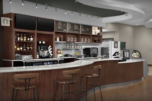 Zona de bar moderna con una barra curva, taburetes y una variedad de bebidas y cristalería.