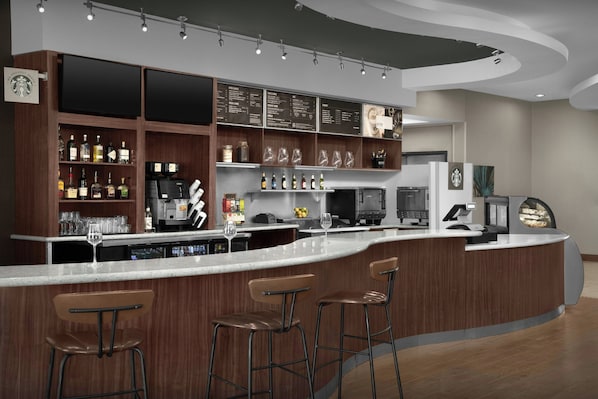 A modern bar area with a curved counter, bar stools, and a variety of beverages and glassware.