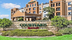 A Courtyard Marriott hotel with a stone facade, multiple balconies, and a landscaped entrance. - Courtyard by Marriott San Antonio SeaWorld - Westover Hills (San Antonio)