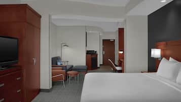 A hotel room with a large bed, a TV, a desk with a chair, a small table, and a sofa.