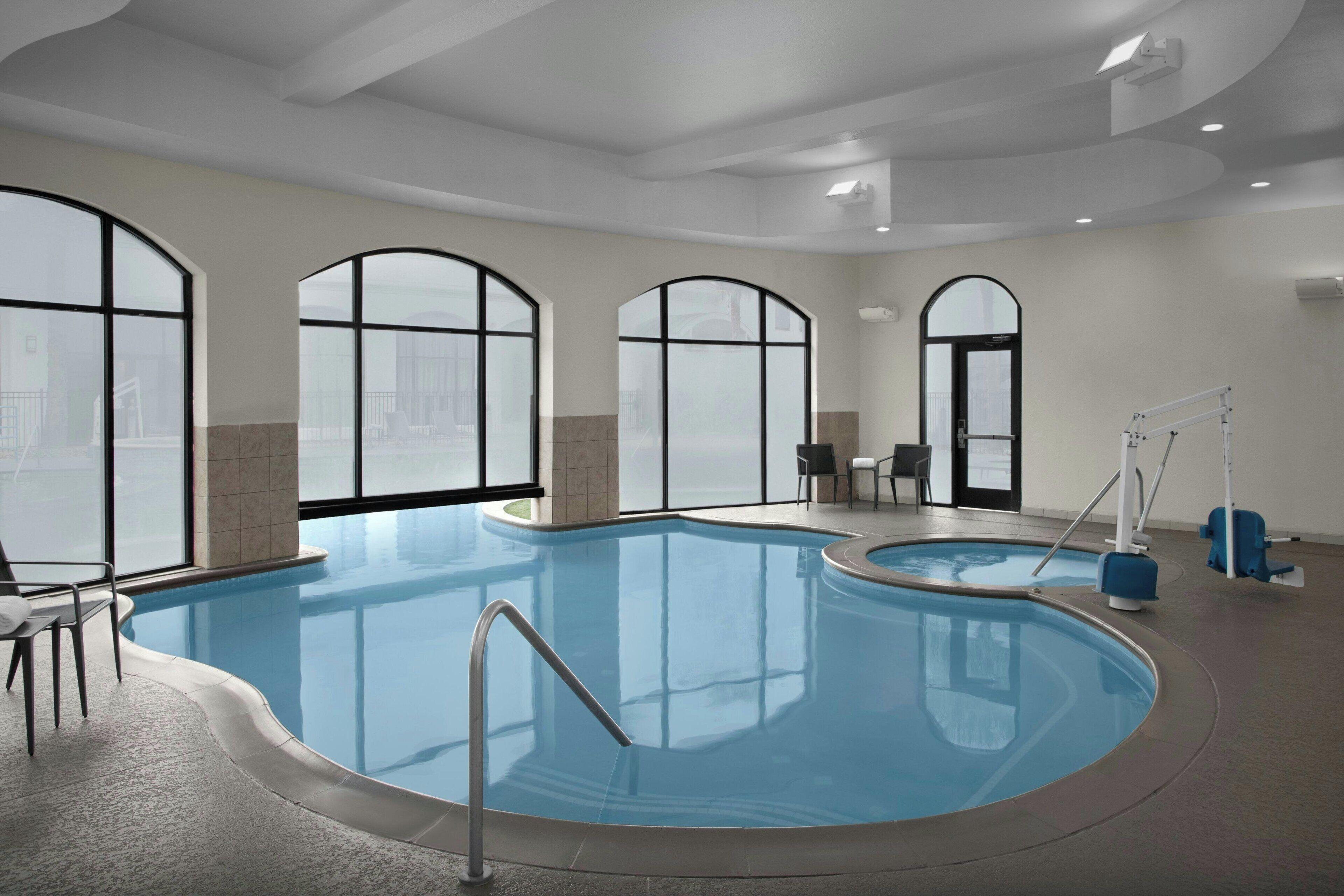 Una amplia piscina cubierta con vista despejada al paisaje urbano a través de grandes ventanales en arco.