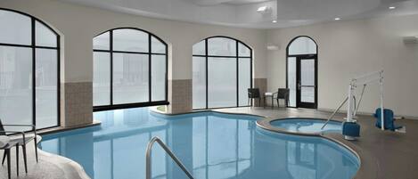 Una amplia piscina cubierta con vista despejada al paisaje urbano a través de grandes ventanales en arco.