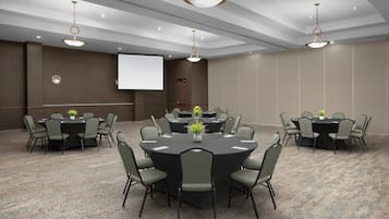 A conference room with round tables, chairs, a projector screen, and ceiling lights.
