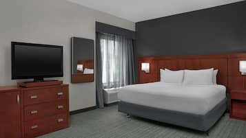 A hotel room with a bed, a television, a dresser, a mirror, and a window with curtains.