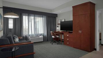 A hotel room with a sofa, a desk, a television, and a wardrobe.