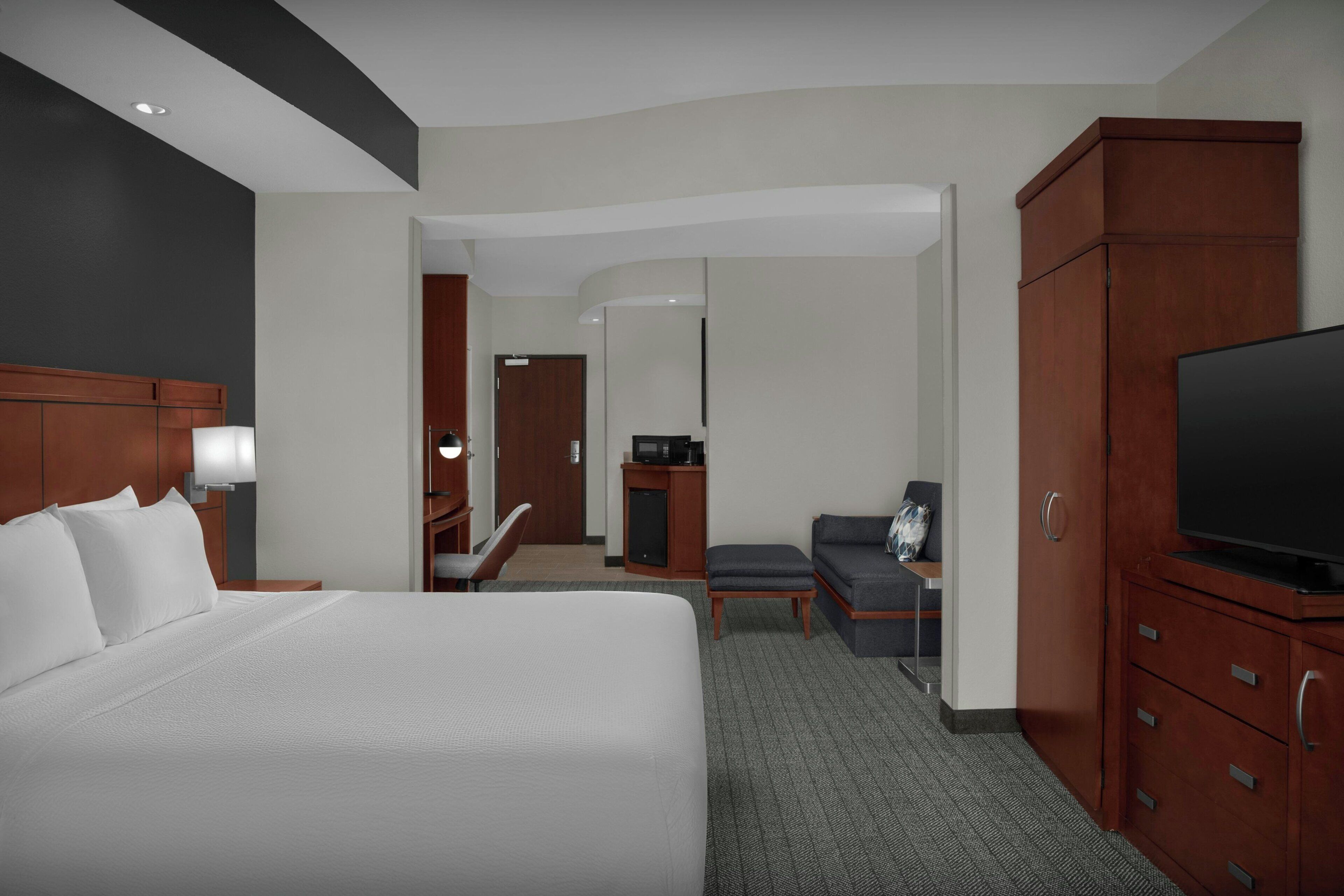 A hotel room with a large bed, a television, a desk with a computer, and a wardrobe.
