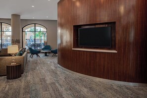 A modern lobby with a wooden reception desk, a flat-screen TV, comfortable seating, and large windows offering a view of the outdoors. - Courtyard by Marriott San Antonio SeaWorld - Westover Hills (San Antonio)