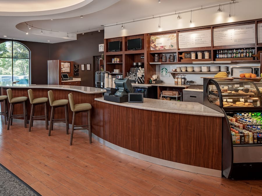 Een moderne koffiebar met een gebogen toonbank, barstoelen, een vitrine met gebak en een menubord.