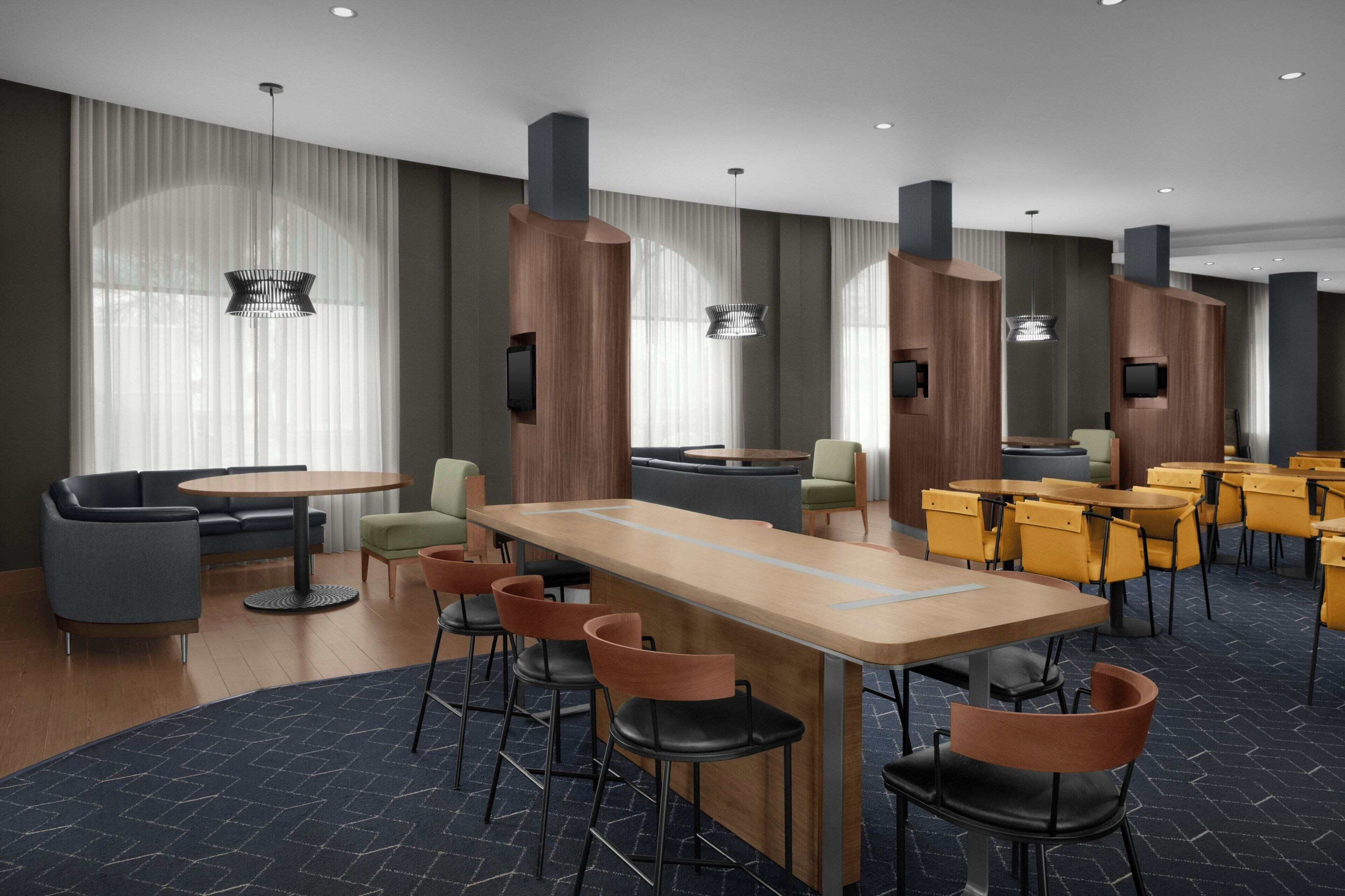 Um lobby de hotel moderno com área de bar central, espaços de estar e grandes janelas com cortinas.