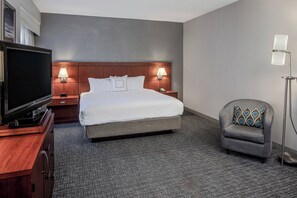 Ein Hotelzimmer mit einem großen Bett, einem Fernseher, zwei Nachttischlampen, einem Sessel und einer Stehlampe.