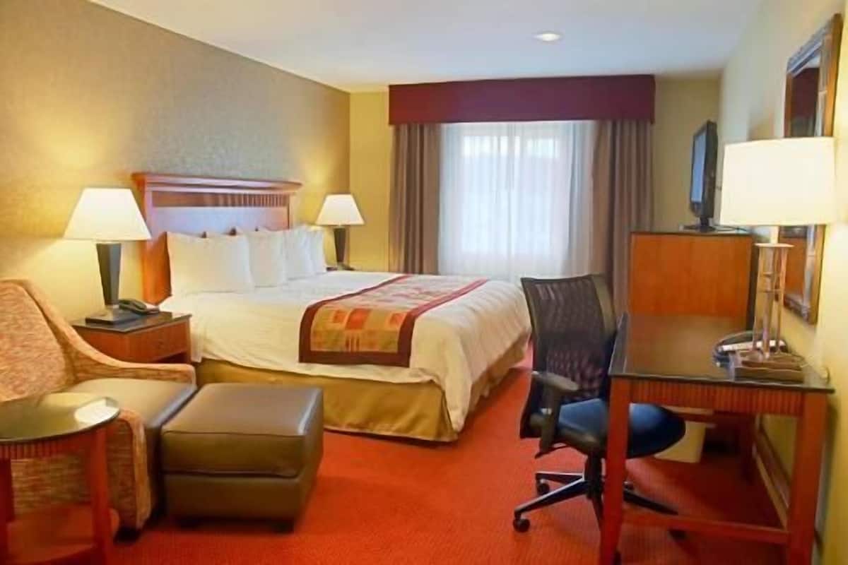 A hotel room with a bed, two bedside lamps, a desk with a chair, a small table, and a television.