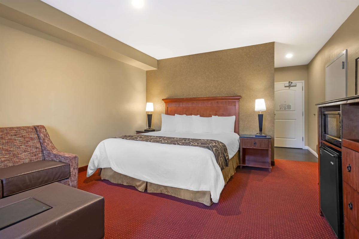 A hotel room with a large bed, two bedside tables with lamps, a small sofa, a refrigerator, and a cabinet.