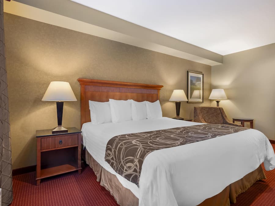 A hotel room with a large bed, two bedside tables with lamps, a chair, and a door.