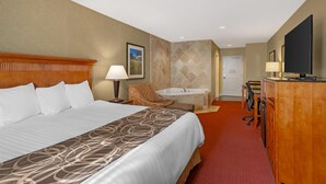 Ein Hotelzimmer mit einem großen Bett, einem Schreibtisch mit Computer, einem Sessel, einem kleinen runden Tisch, einer Badewanne und einem Fernseher.