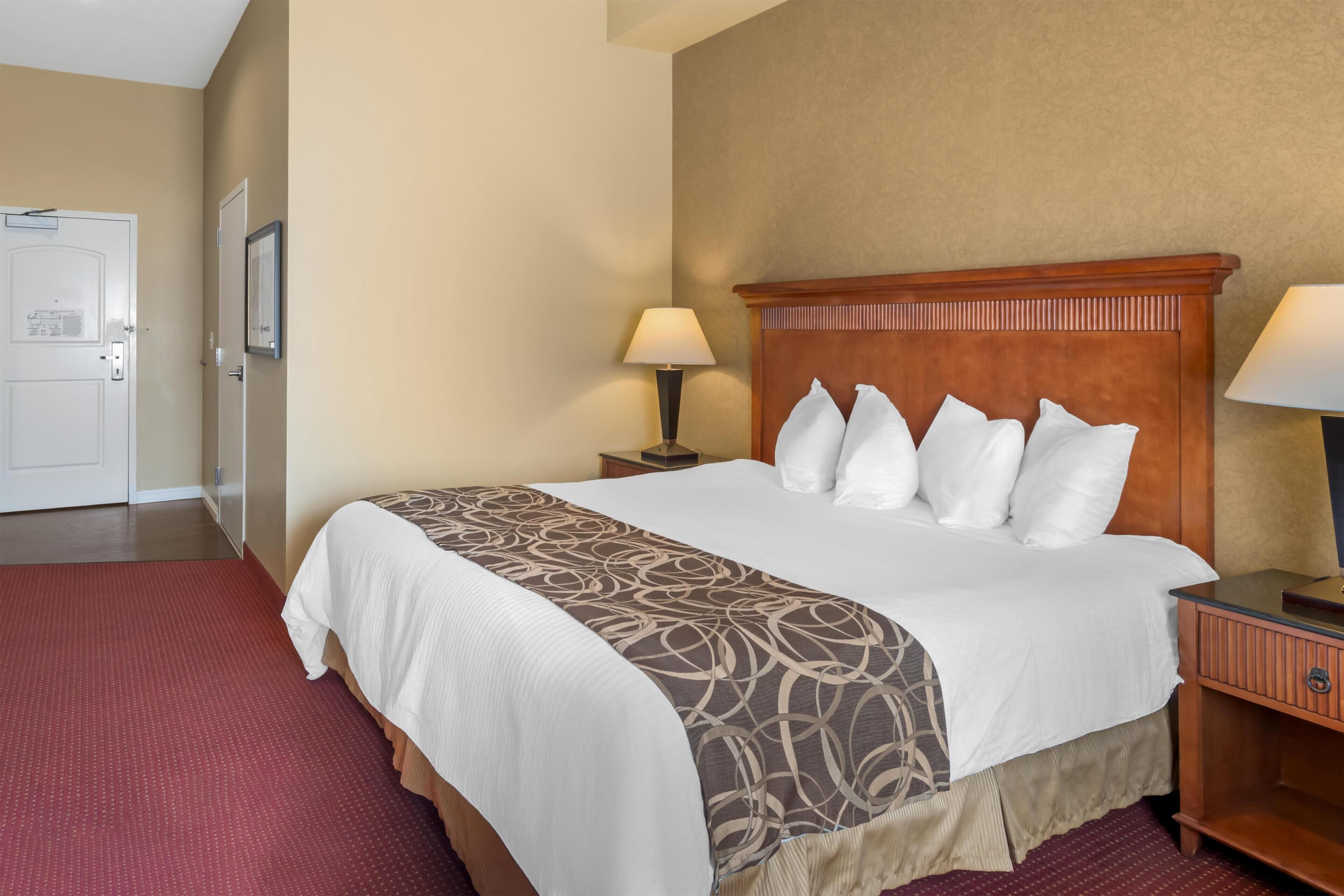 A hotel room with a large bed, two bedside tables, a door, and a wall-mounted lamp.