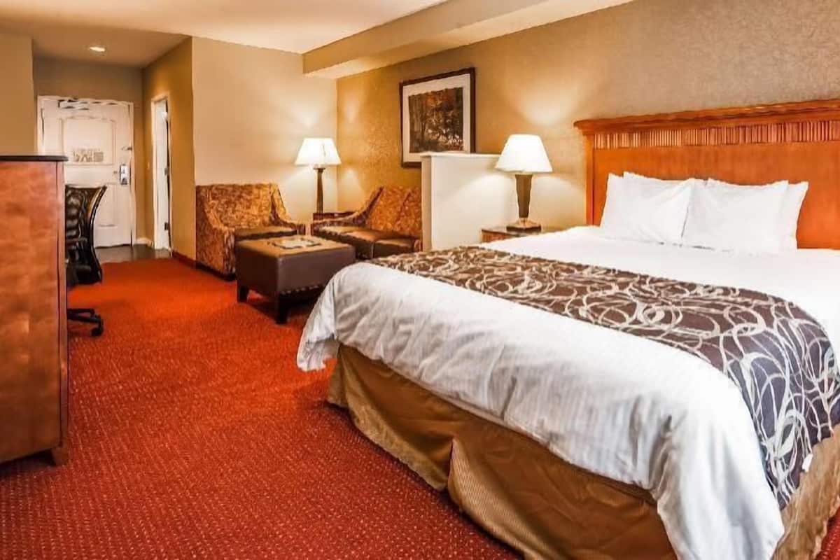 A hotel room with a large bed, two bedside tables with lamps, a sofa, a desk, and a chair.