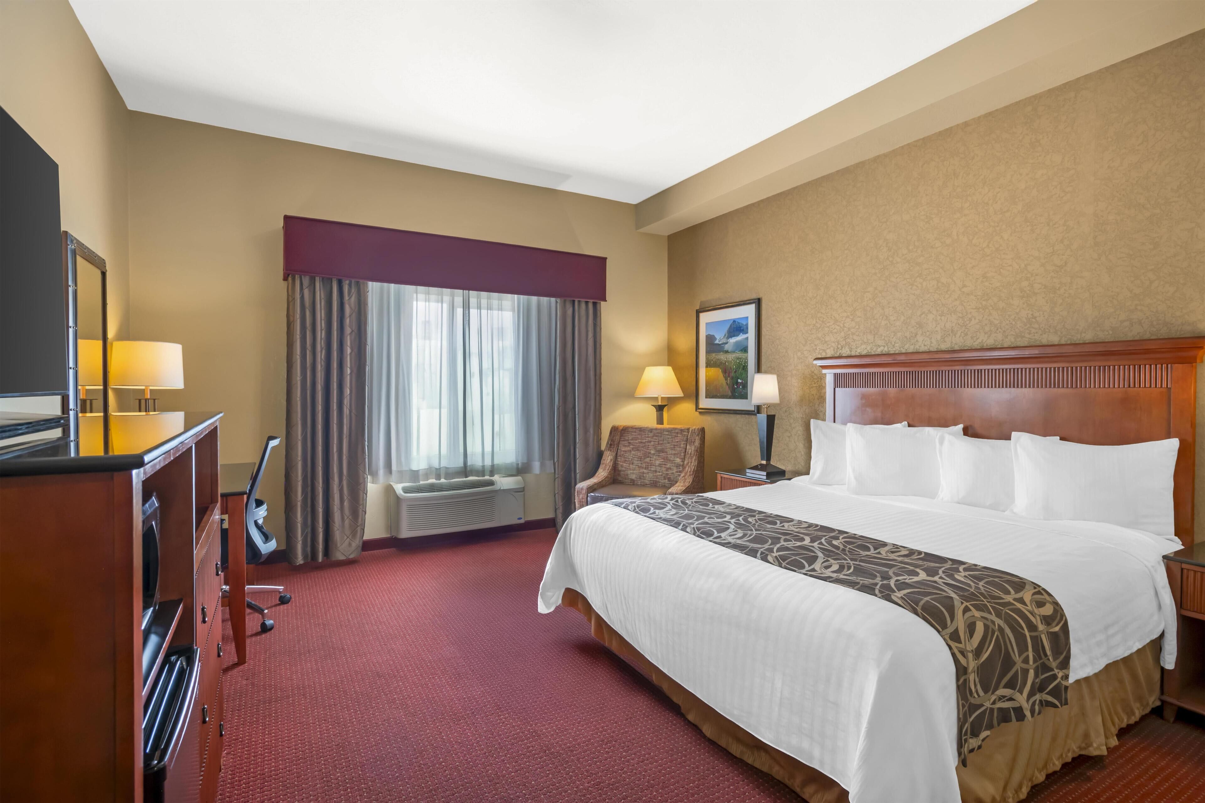 A hotel room with a large bed, a desk with a mirror, a chair, a window with curtains, and a painting on the wall.