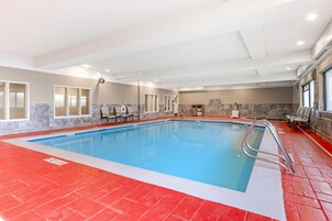 Una piscina interior con suelo rojo, agua azul cristalina y una zona de estar con sillas.