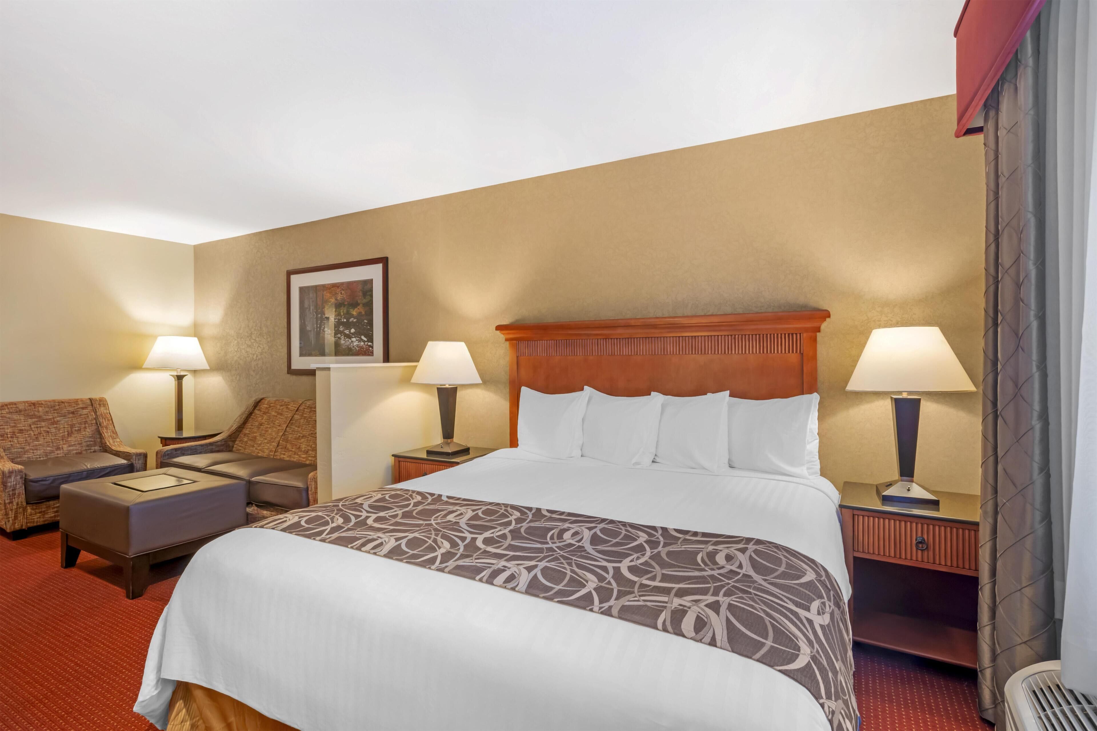 A hotel room with a large bed, two bedside tables with lamps, a sofa, and a small table.