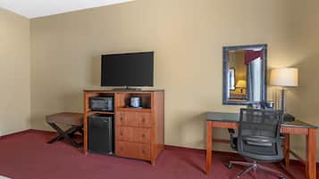 A hotel room with a bed, a desk with a computer, a television, a small refrigerator, a microwave, a chair, and a mirror.