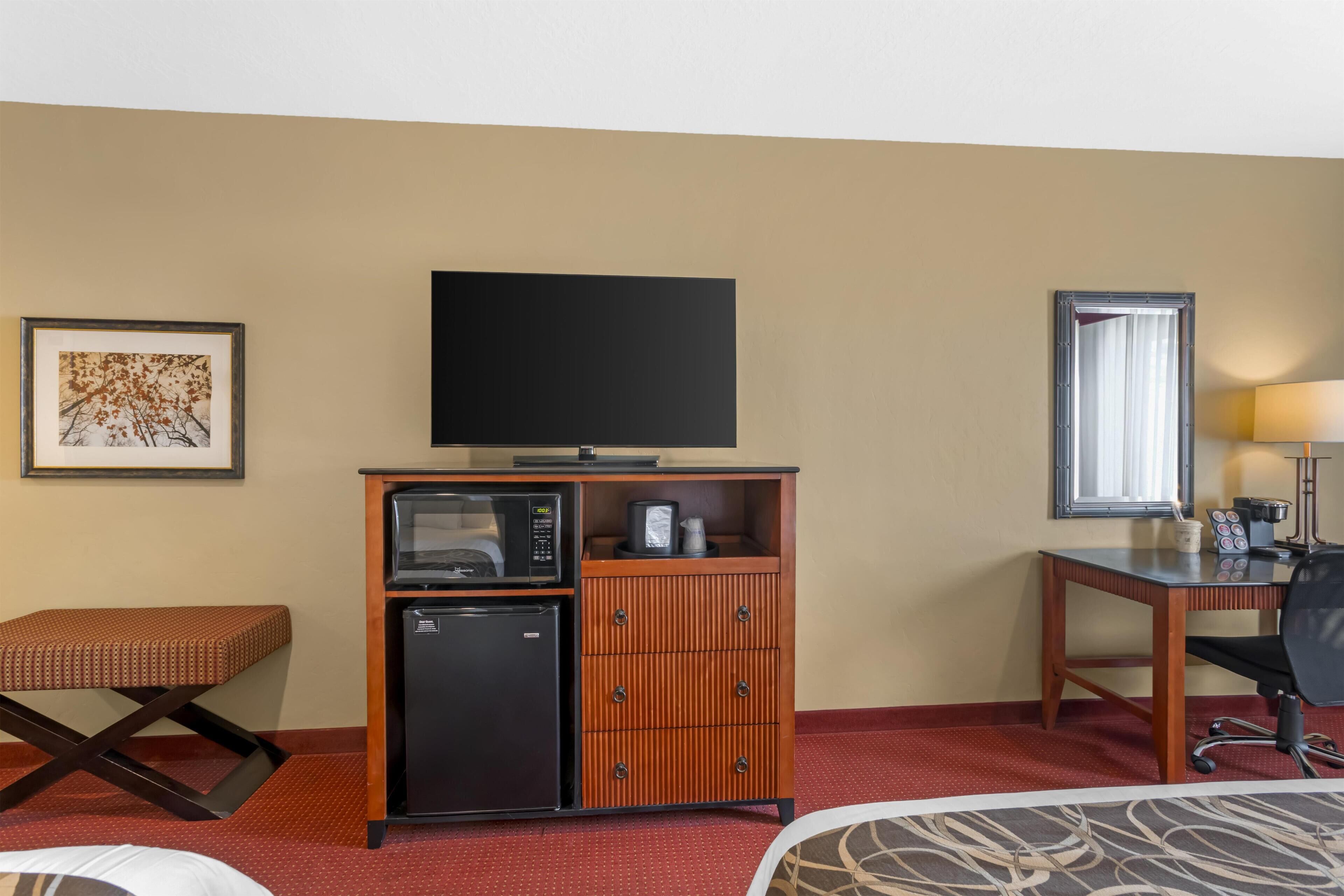 A hotel room with a bed, a desk with a chair, a television, a minibar, and a small refrigerator.