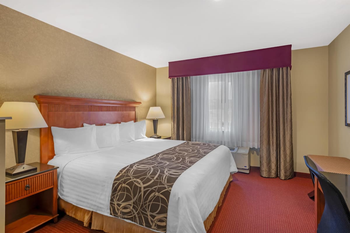 A hotel room with a large bed, two bedside lamps, a desk, and a window with curtains.