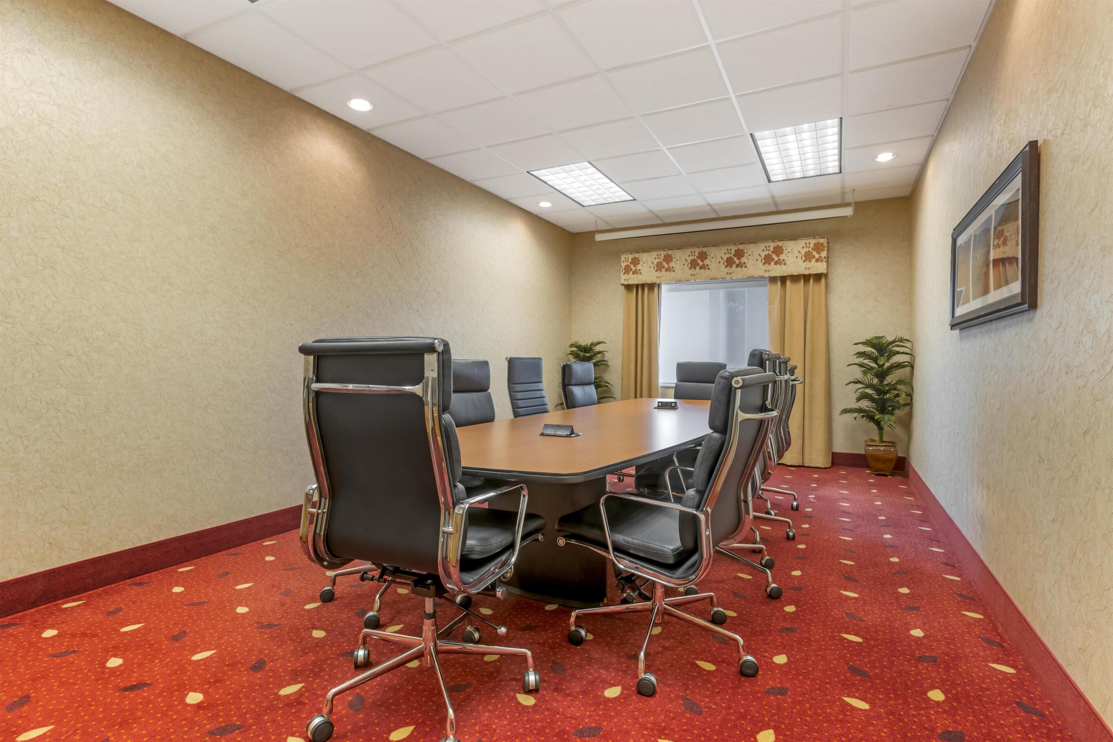 A conference room with a large table, six chairs, and a potted plant.