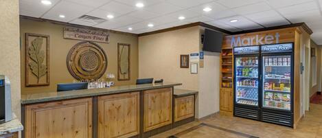 A reception area with a wooden reception desk, a wall-mounted sign reading "Canyon Pines," and a "Market" refrigerator stocked with beverages and frozen food.