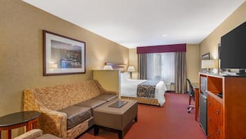 Une chambre d’hôtel avec un canapé, une petite table, un lit recouvert d’une couvre-lit à motifs, un bureau avec une télévision et une fenêtre avec des rideaux.