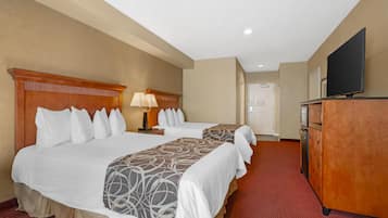 A hotel room with two beds, a dresser, a television, and a door.