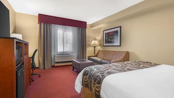 A hotel room with a bed, a desk, a chair, a lamp, a picture on the wall, and a window with curtains.