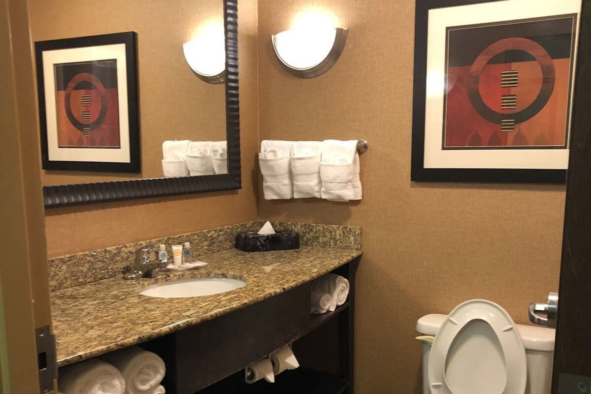 A bathroom with a granite countertop sink, a toilet, a mirror, and framed artwork on the walls.