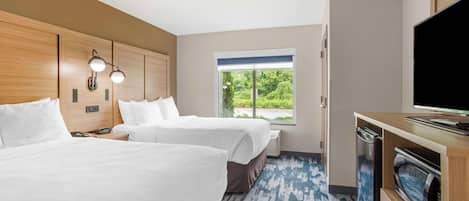 A hotel room with two beds, a television, a microwave, and a large window with a view of greenery.