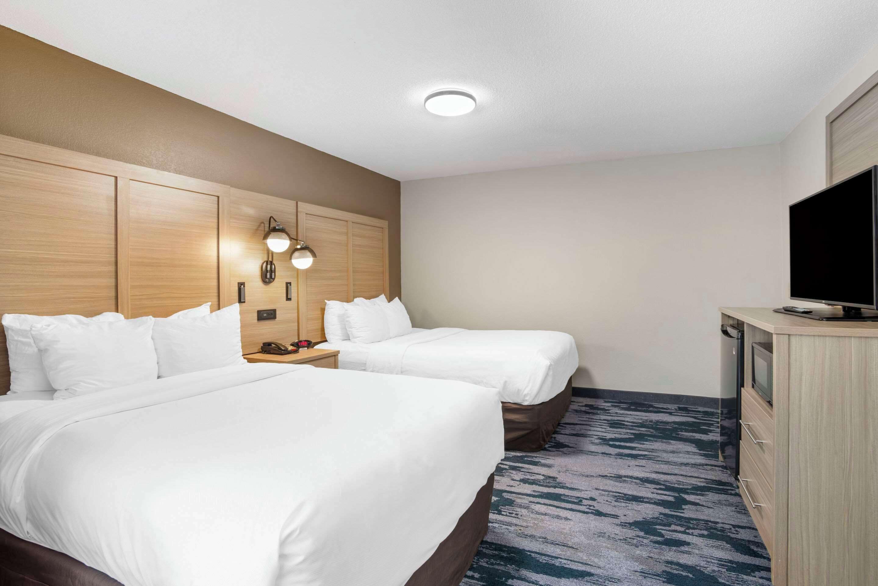A hotel room with two beds, a desk with a TV, and a wall-mounted light fixture.