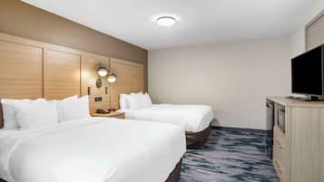 A hotel room with two beds, a desk with a TV, and a wall-mounted light fixture.