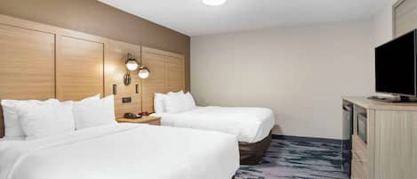 Habitación de hotel con dos camas, un escritorio con televisor y una lámpara fijada a la pared.